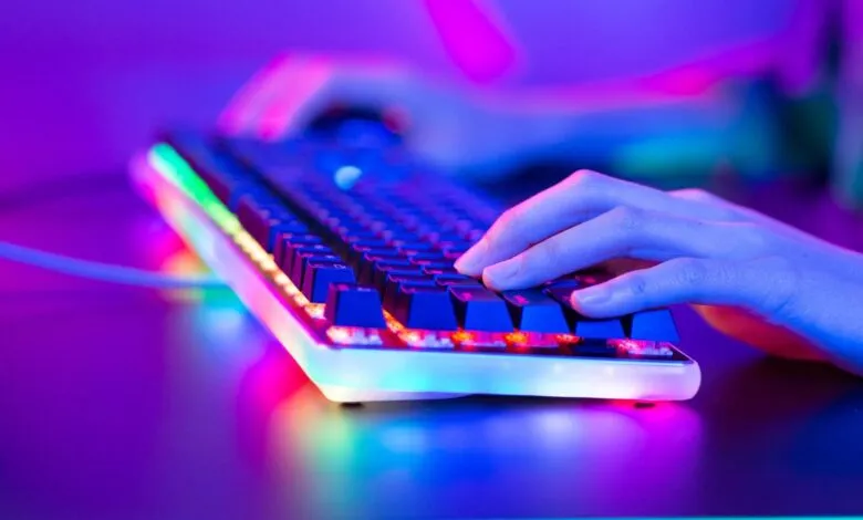 Hands type on a backlit gaming keyboard with vibrant RGB lighting.