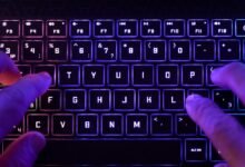 Hands typing on a backlit keyboard with colorful RGB lighting.