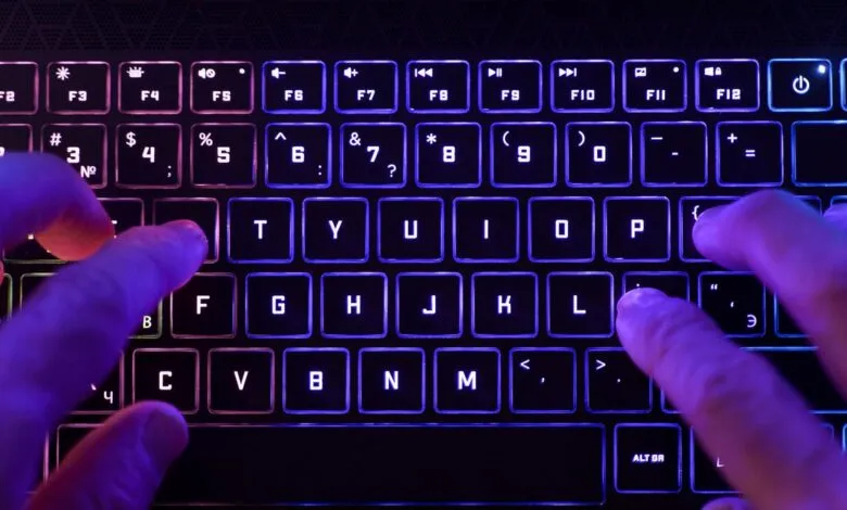 Hands typing on a backlit keyboard with colorful RGB lighting.