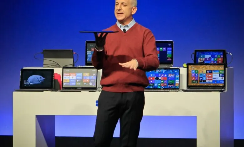 Man presenting tablet with laptops on display table.