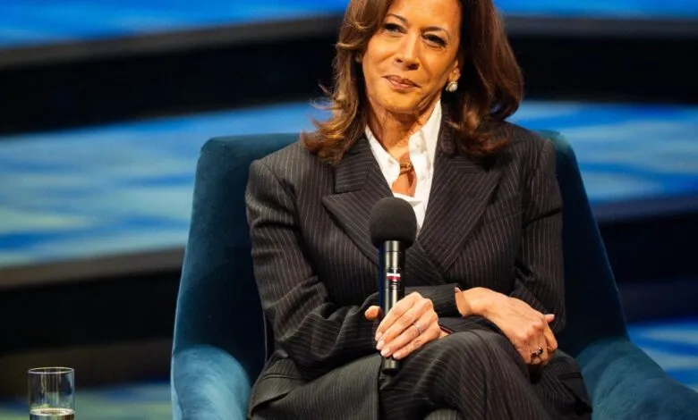 Kamala Harris sits in a blue chair, holding a microphone.