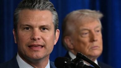 Man speaks at podium with Donald Trump in background.