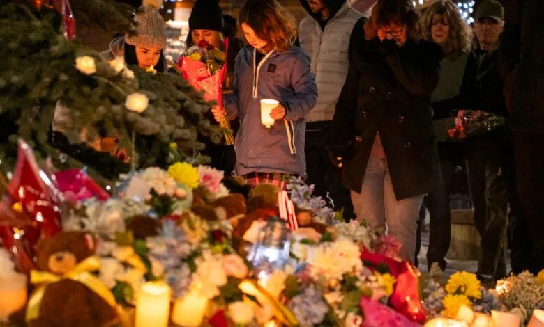 Mourners gather at memorial with flowers, candles, and teddy bears.