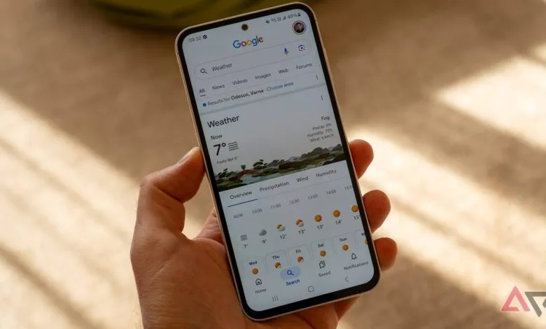 Hand holding phone displaying Google Weather app with current conditions.