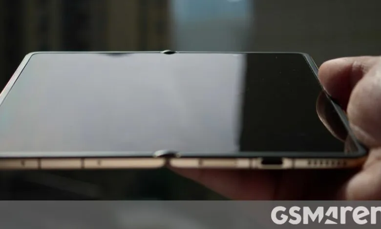 Foldable smartphone held in hand, showing hinge and reflective screen.