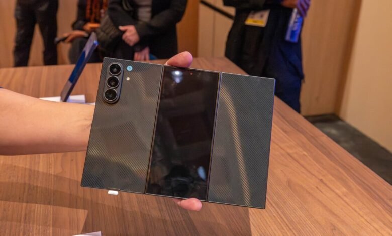 Hand holding a foldable smartphone with a textured back and triple camera system.