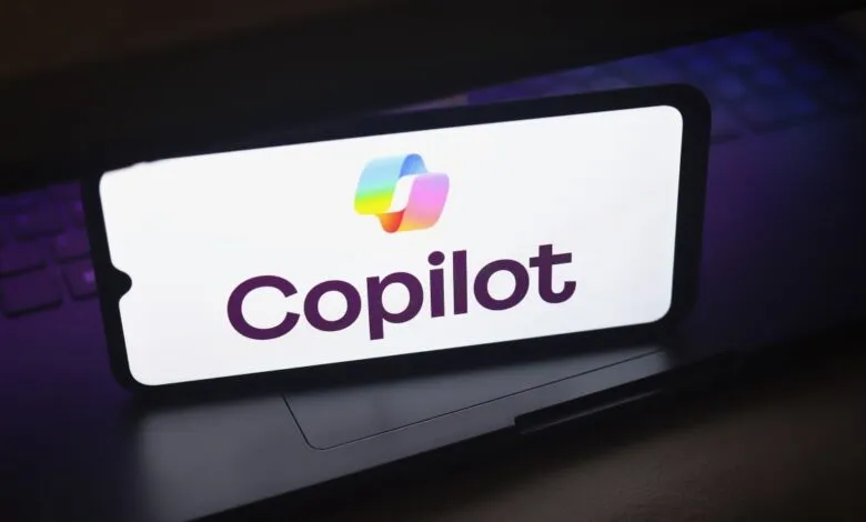 Phone displays the Copilot logo, a colorful ribbon, on a laptop.