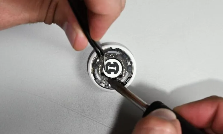 Close-up of an AirTag being disassembled with tweezers and a screwdriver.