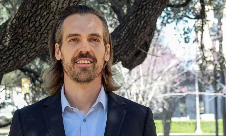Smiling man with long hair and beard in suit jacket outdoors.