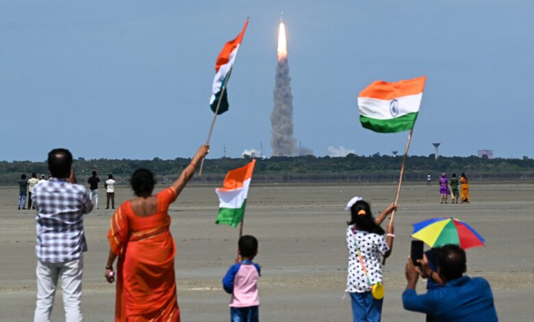 People wave Indian flags as a rocket launches into the sky, celebrating space exploration.