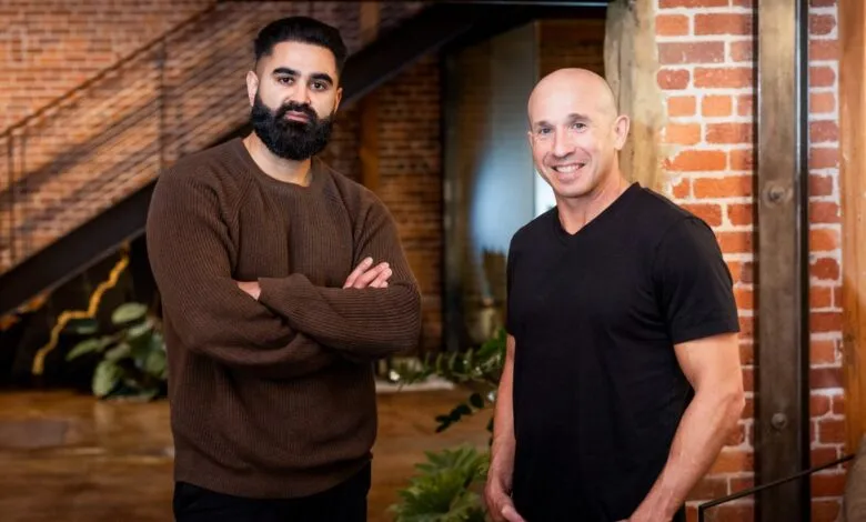 Two men stand in a modern office space with exposed brick and metal beams.