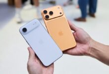 Two iPhones, one gold with three cameras, one light blue with one camera, held in a hand.