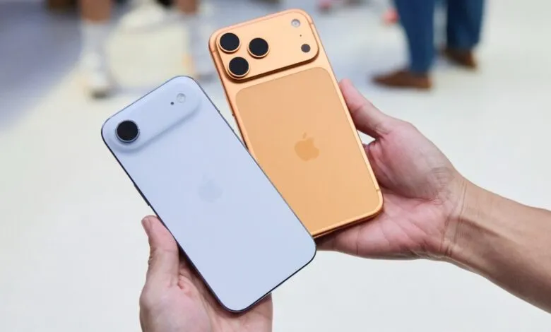 Two iPhones, one gold with three cameras, one light blue with one camera, held in a hand.