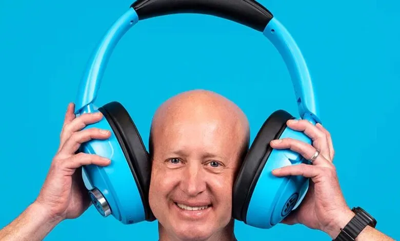 Man holds oversized blue headphones against a bright blue background.