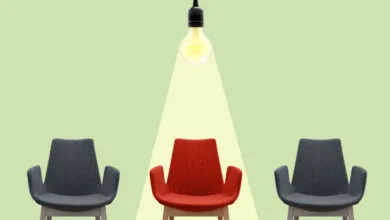 Three chairs, one red under a spotlight, two gray on either side.