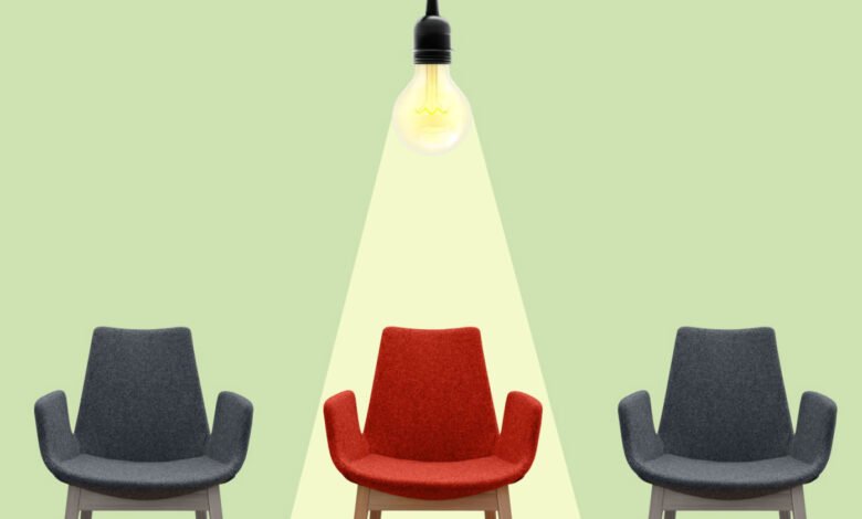 Three chairs, one red under a spotlight, two gray on either side.