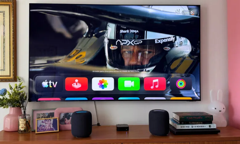Apple TV displaying racing driver with app icons, HomePods on wooden console.