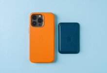 Orange iPhone in case next to blue MagSafe wallet on light blue background.