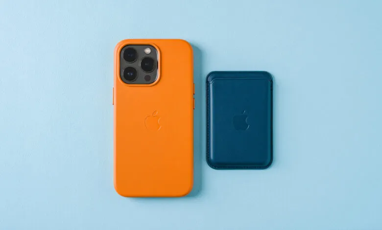 Orange iPhone in case next to blue MagSafe wallet on light blue background.