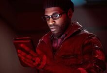 Man with glasses and beanie intently looks at a tablet in red lighting.