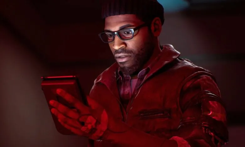 Man with glasses and beanie intently looks at a tablet in red lighting.