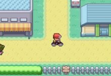 Pixelated game scene with character on bike, buildings, and grassy areas.