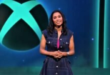 Woman in denim dress stands before Xbox logo on blue background.