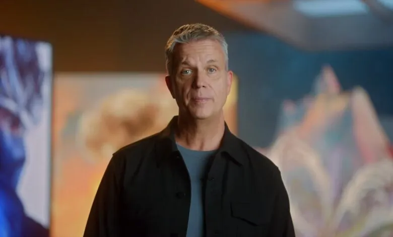 Man with gray hair and blue eyes stands in front of abstract art.