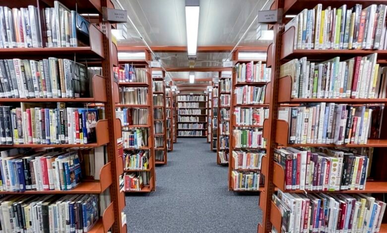 Library aisle with tall shelves filled with books, gray carpet.