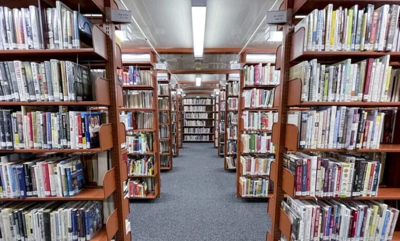 Library aisle with tall shelves filled with books, gray carpet.