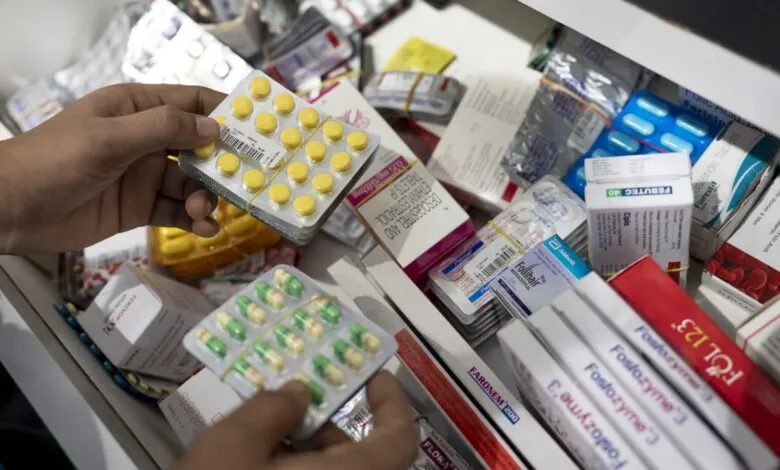 Hands holding blister packs of yellow and green pills over a drawer full of medications.