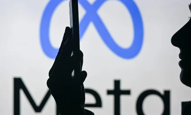 Silhouette of person holding phone in front of Meta logo.
