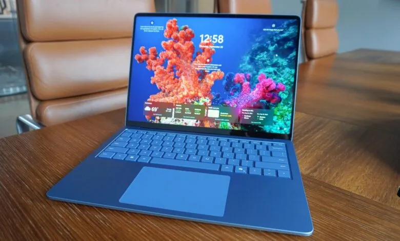 Blue Microsoft Surface Laptop on a wooden desk, screen displaying coral reef.