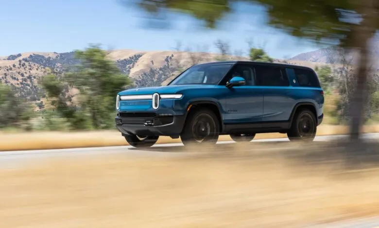 Blue Rivian R1S SUV driving on a road with blurred background.