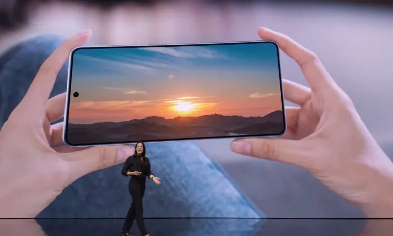 Woman presenting a new smartphone displaying a sunset landscape.