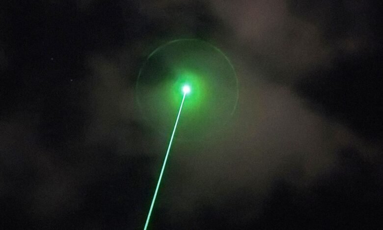 Bright green laser beam piercing through dark, cloudy night sky.
