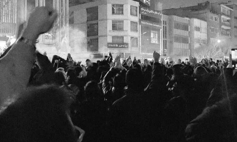 Black and white photo of a crowd protesting at night, raising hands.