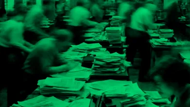 Blurred image of people working at desks covered in stacks of papers, green filter.