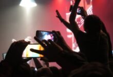 Concert crowd recording performance with smartphones in a dark, smoky venue.