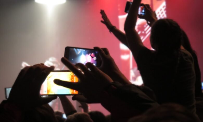 Concert crowd recording performance with smartphones in a dark, smoky venue.