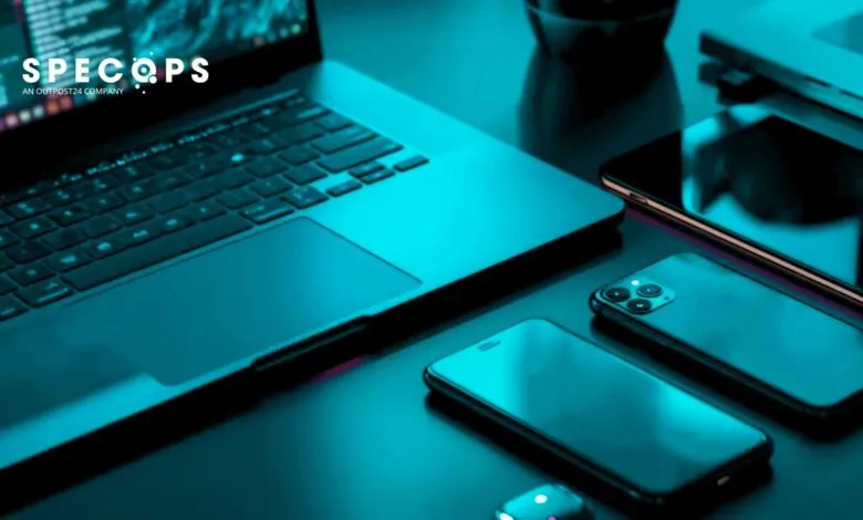 Laptop and multiple smartphones arranged on a dark surface, lit with teal lighting.