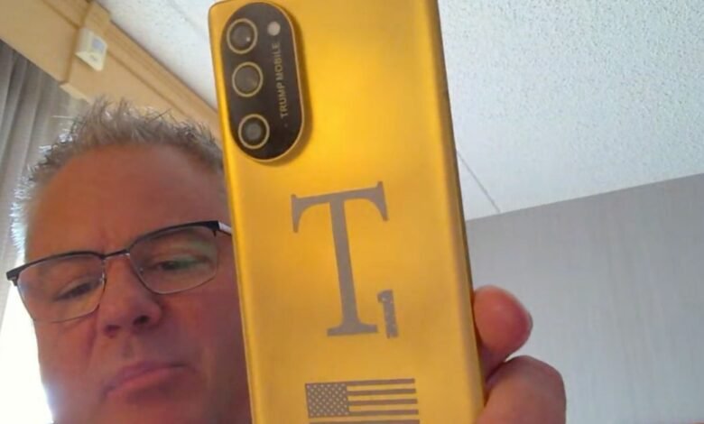 Man holds up a gold phone with 'Trump Mobile' and an American flag design.