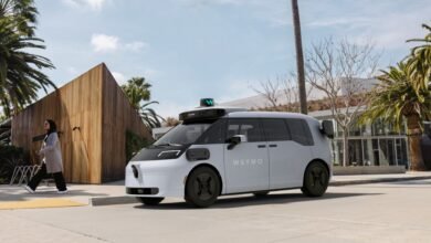 Waymo self-driving car parked near a woman walking on a sunny street.
