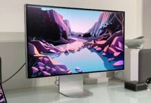 Studio Display showing landscape art, with laptop, speakers, and decorative objects.