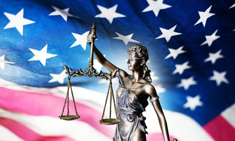 Statue of Lady Justice with scales against an American flag backdrop.