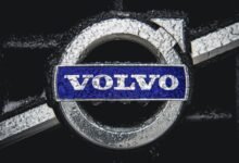 Close-up of Volvo logo with water droplets on a dark background.