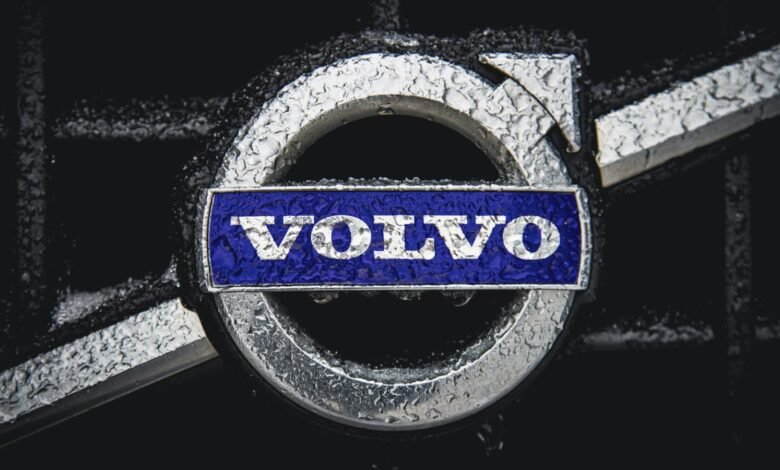 Close-up of Volvo logo with water droplets on a dark background.