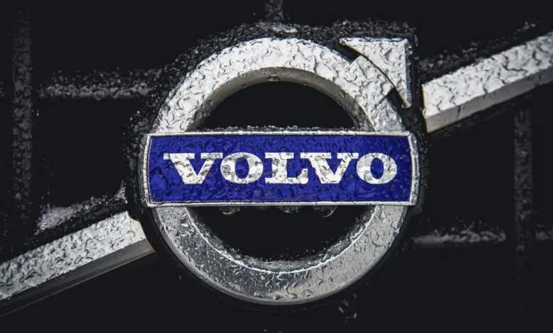 Close-up of Volvo logo with water droplets on a dark background.