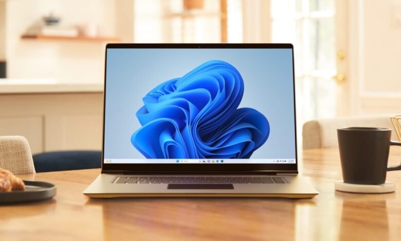 Laptop displaying Windows 11 desktop with coffee cup and pastry on wooden table.