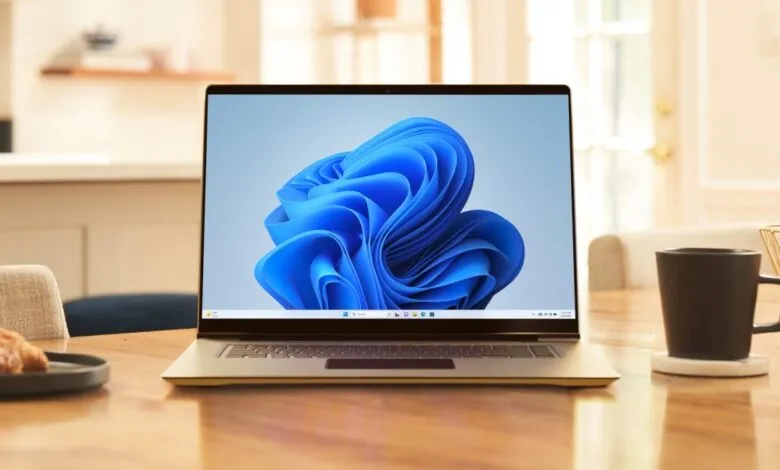 Laptop displaying Windows 11 desktop with coffee cup and pastry on wooden table.